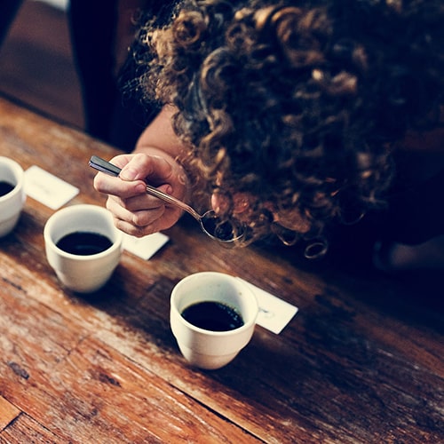 Person Using a Spoon to Taste Coffee in a Cupping Session