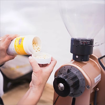 How to Clean a Coffee Grinder — Pouring Coffee Grinder Cleaning Tablets into the Bottle’s Lid Before Use