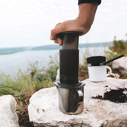 Adventure and Coffee — Brewing Coffee with AeroPress at Lakeside Camp Traveler Using AeroPress on Metal Mug by a Lake