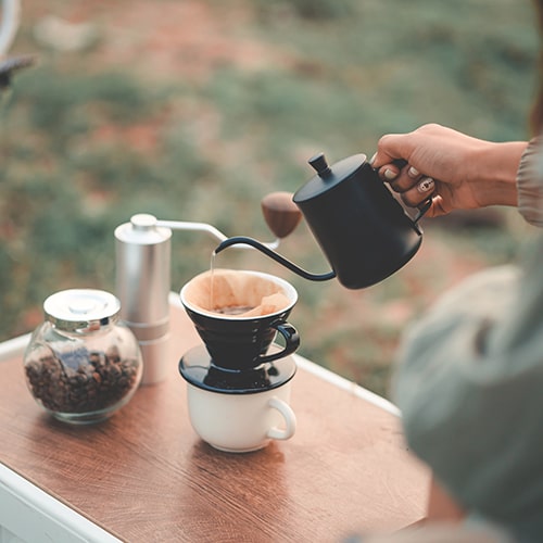 Adventure and Coffee — Pour-Over Coffee in the Wilderness A Person Pouring Hot Water for Pour-Over Coffee at a Campsite