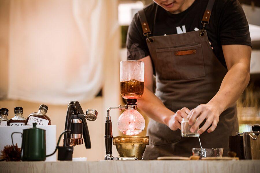 A Barista in an Apron Prepares Coffee Using a Siphon Coffee Maker at a Café Station