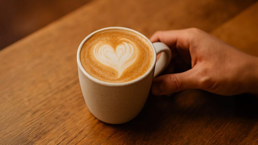 Latte Art Challenge — A Close-Up of a Latte in a Speckled Ceramic Mug with an Imperfect Heart Design, Held Gently on a Wooden Surface